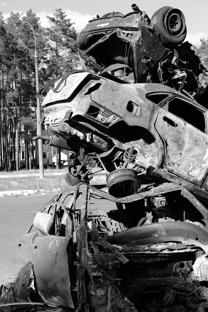 Vertical black-and-white photo of stacked junked cars in an outdoor scrapyard.
