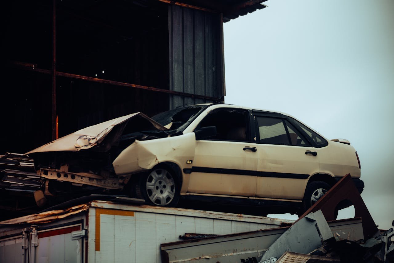 heros-img A damaged car sits atop a metal scrap heap, showing a scene of automotive decay.