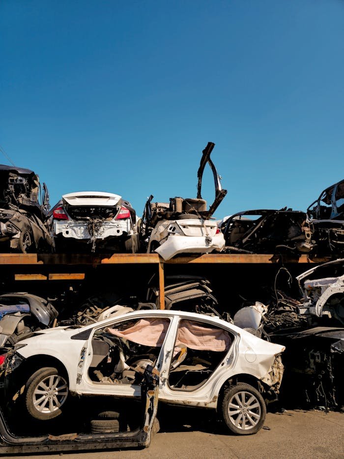 services-01 Rows of damaged vehicles in a scrapyard under a clear blue sky.